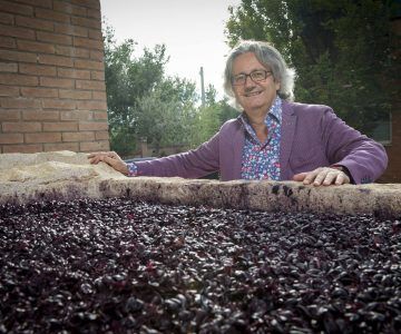 Winemaker of Chiusa Grande leaning on a vat of dark grapes, smiling.