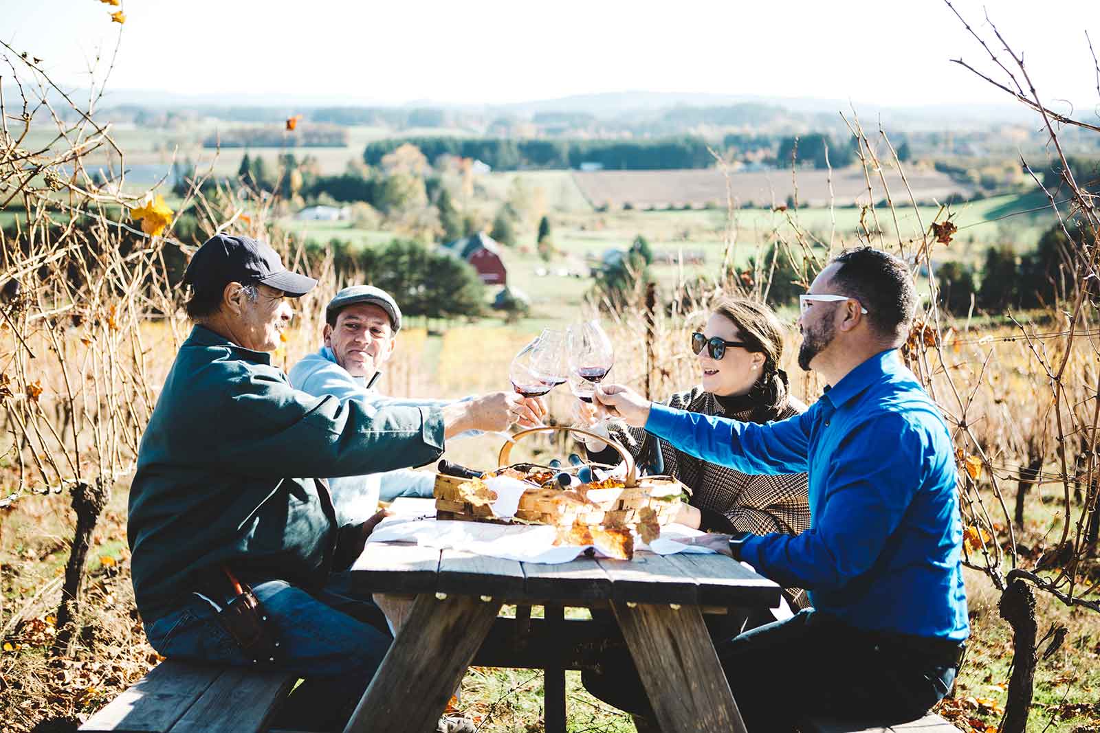 Four people clink wine glasses at a picnic table overlooking Cooper Mountain vineyard
