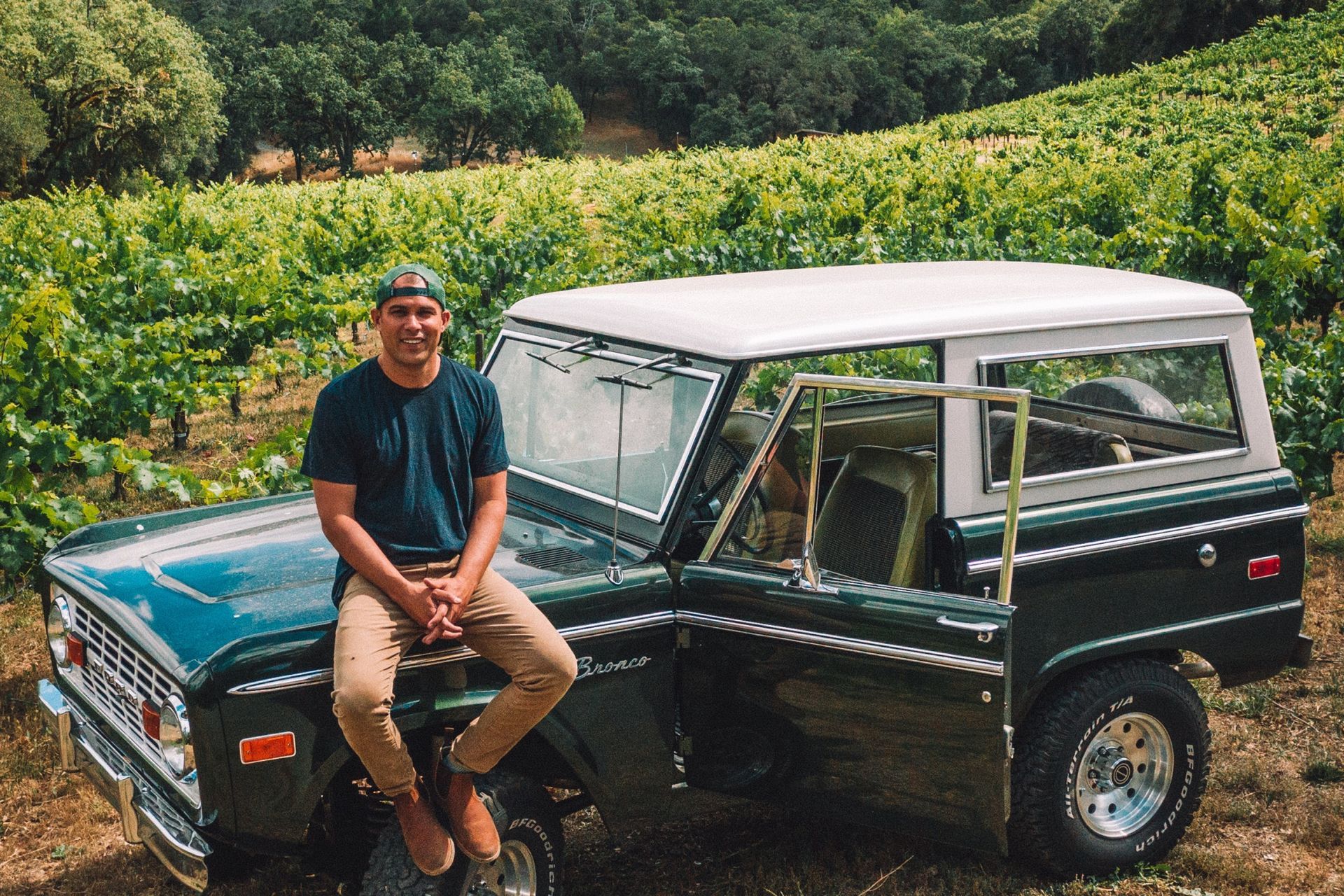 Winemaker sitting on a green Bronco car, with the Grounded Wine Co. vineyard on the background.