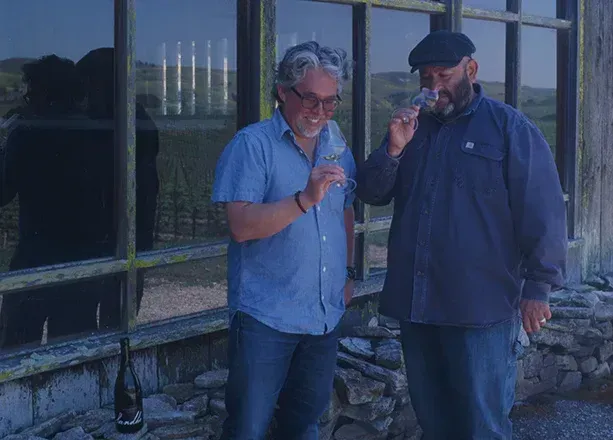 Two men examining wine in glasses outside Sandhi Winery