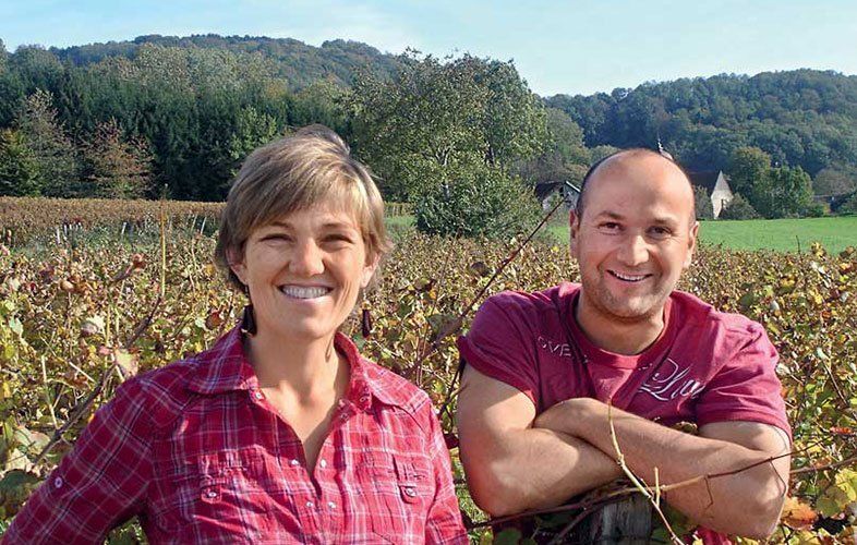 Tissot winemakers smiling in a vineyard; trees and a blue sky in the background.