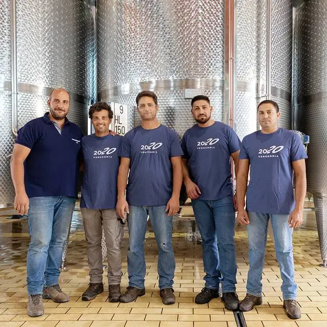 Di Giovanna team stand in the winery, posing in front of large metal tanks.