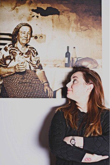 Woman looking at a framed sepia-toned photograph of an older woman sitting at a table.