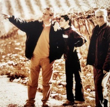 Three men outside at Chiusa Grande vineyard. One points, another leans, the third watches. Sepia tone.