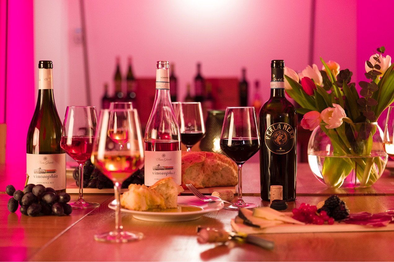 Table setting with Chiusa Grande wine bottles, glasses, food, and flowers under pink lighting.